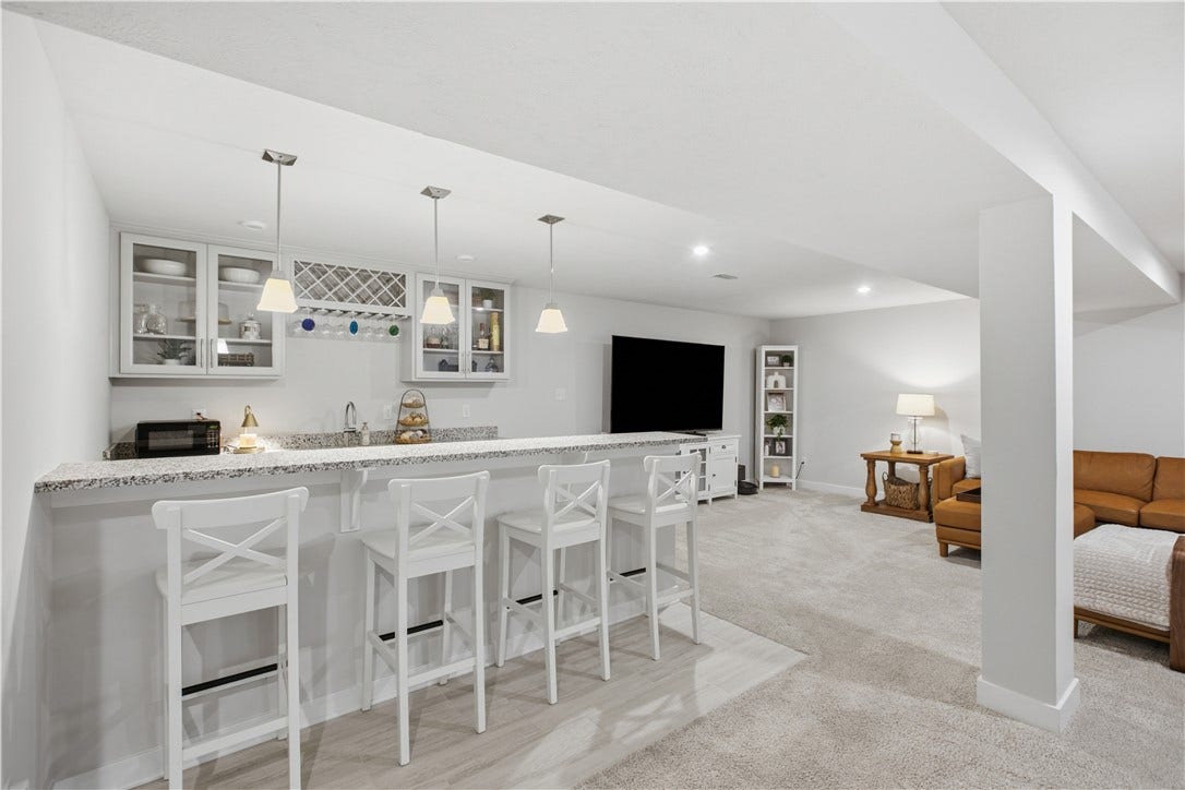 Stylish wet bar showcases granite countertops, extensive cabinetry, glass-front display cabinets, built-in wine storage, pendant lighting, and an oversized peninsula with seating.