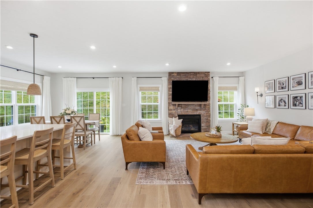 Open-concept great room features stone gas fireplace, abundant windows, and seamless kitchen and dining flow.