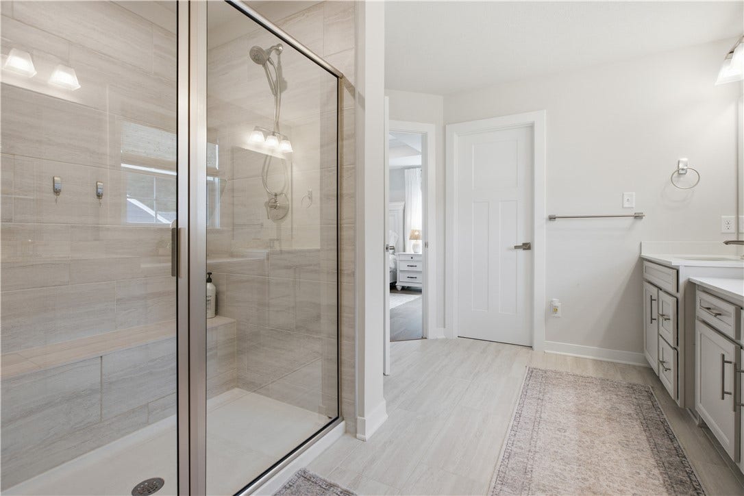 Showcasing an oversized tiled shower with glass enclosure, built-in bench, and dual vanity.