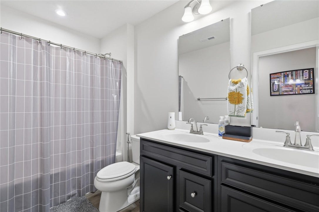The upper-level full bath features a fiberglass tub, double vanity with dual mirrors, and luxury vinyl flooring paired with sleek black raised-panel cabinetry.