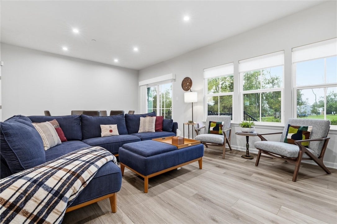 This inviting 14'14' living room features a wall of windows, a slider to the deck, and abundant natural light that enhances its tall 9' ceilings.