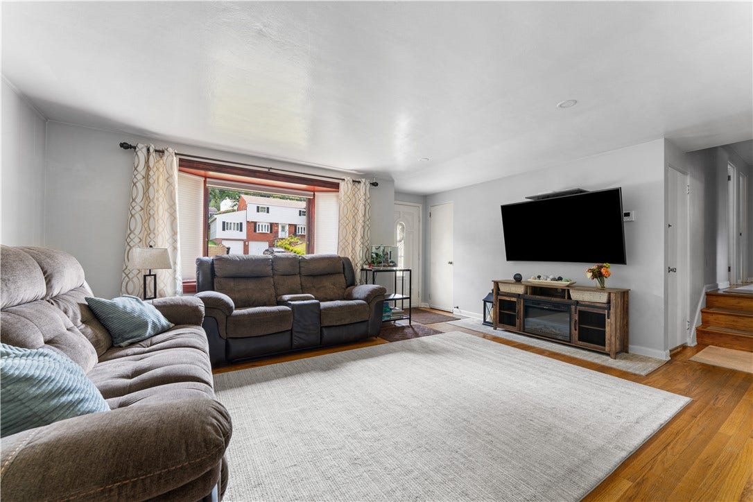 The spacious living room features hardwood floors, a large bay window with remote-controlled blinds, and a neutral color palette suitable for any decor.