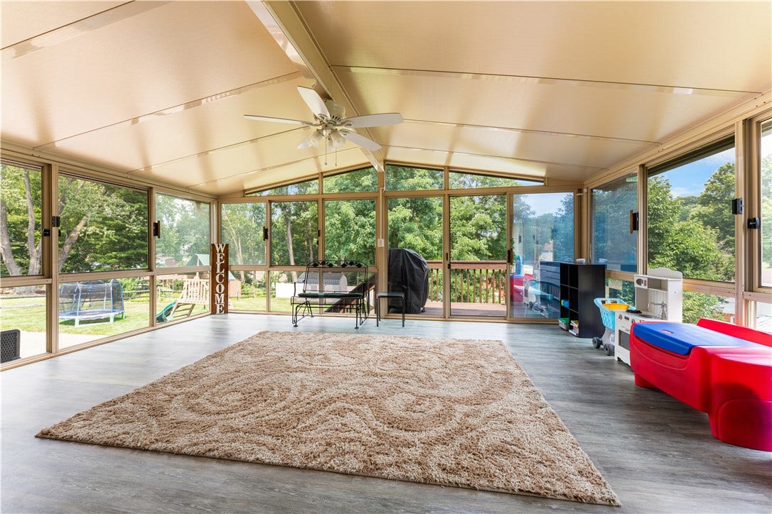 Spacious three-season sunroom featuring ceiling fan and expansive window walls, perfect for relaxing and entertaining.