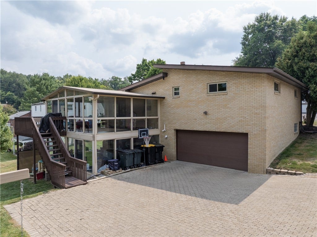 This view of the rear exterior highlights the additional living space provided by the sun rooms, as well as the Omni Stone driveway and two-car garage.