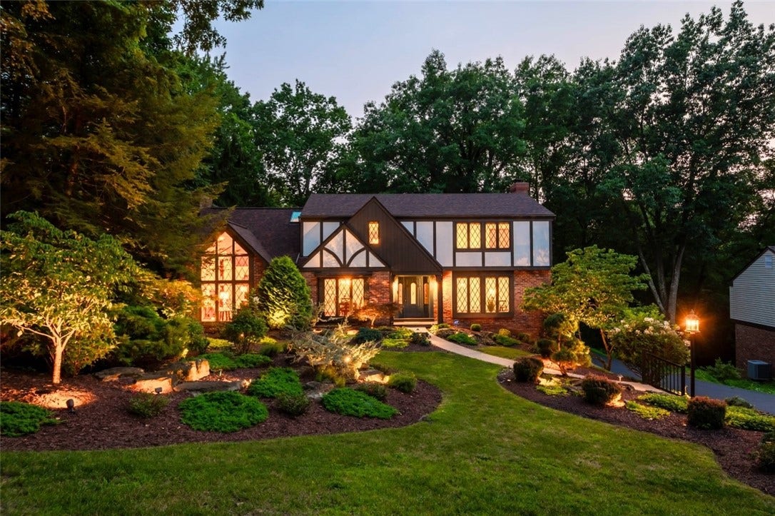 Timeless Tudor architecture framed by mature trees and beautifully illuminated landscaping creates an unforgettable first impression.