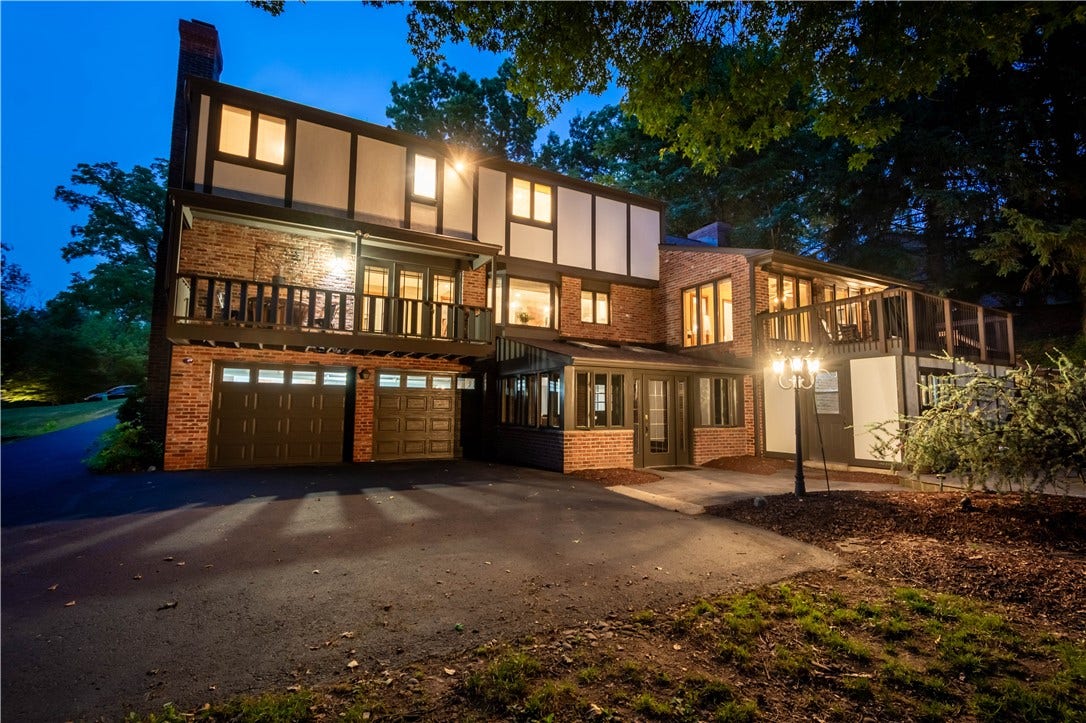 The home's expansive rear elevation comes alive at dusk, showcasing multiple levels of outdoor living.