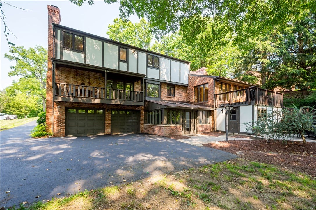 Expansive outdoor living spaces extend across the rear of the home, surrounded by the privacy of mature trees.