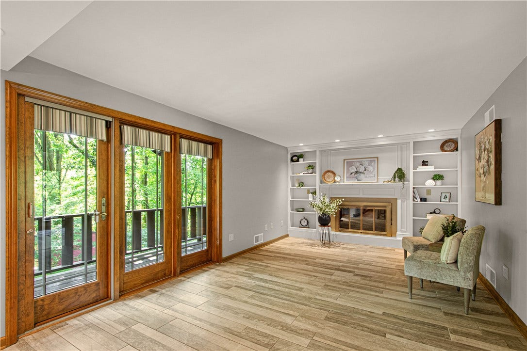 A warm, welcoming living space with custom built-ins, fireplace, and walls of windows overlooking the greenery beyond.