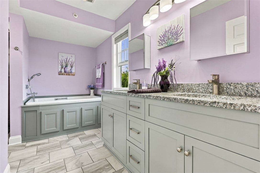 Luxurious primary en suite featuring dual vanities with granite countertops, tile flooring and a spacious soaking tub.